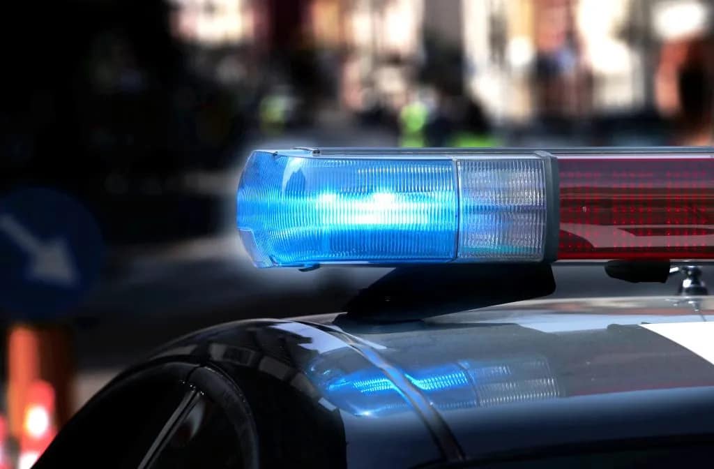 Close-up of a police car's flashing blue and red lights, with a blurred urban background.
