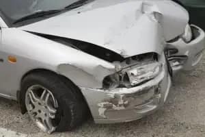 Un automóvil plateado con daños significativos en su parachoques delantero y capó, indicando una colisión reciente. El faro delantero derecho está roto, y otro vehículo es visible junto a él.
