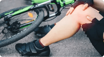 A person sits on the ground next to a green bicycle, holding their injured knee with both hands, suggesting a recent fall—reminding us how unexpected accidents can happen, similar to car accidents that often require lawyers for support.