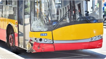 A yellow and red city bus with a damaged front bumper and cracked windshield is parked on a street in daylight, highlighting the aftermath of car accidents that may require the assistance of a personal injury attorney.