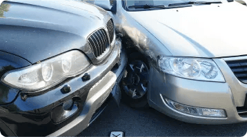 Two cars have collided at the front corners, with the black SUV’s left headlight area pressed against the silver sedan’s right headlight area—an example of car accidents where personal injury lawyers may be needed. Both vehicles are angled on a paved road.