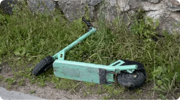 A damaged green electric scooter lies on its side in the grass near a stone wall, with the handlebar and wheels visible—an image that highlights why consulting a personal injury or car accident attorney can be crucial after such incidents.