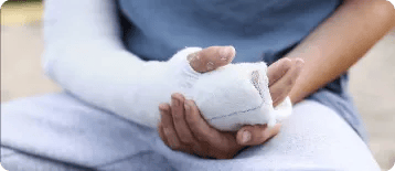 A person wearing a blue shirt and gray pants holds their arm, which is wrapped in a white plaster cast, resting in their lap—perhaps reflecting on whether to consult a personal injury attorney.