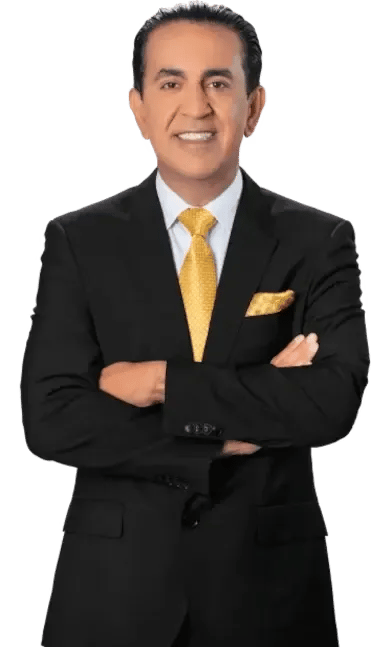 A man in a black suit with a yellow tie and matching pocket square stands with arms crossed, smiling at the camera.