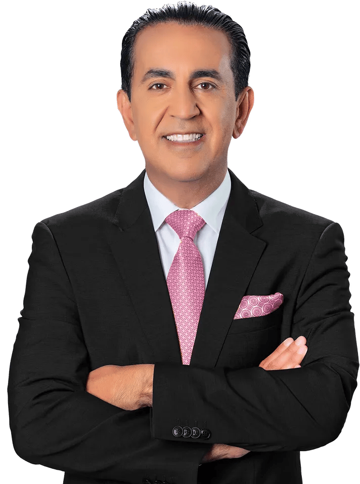 A car accident attorney in a black suit, white shirt, and pink patterned tie stands with his arms crossed, smiling at the camera. He has short dark hair and a matching pink pocket square against a plain white background.