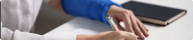 A person wearing a blue sleeve writes on paper with a pen at a desk, possibly jotting down details about car accidents, while a closed black notebook lies nearby.