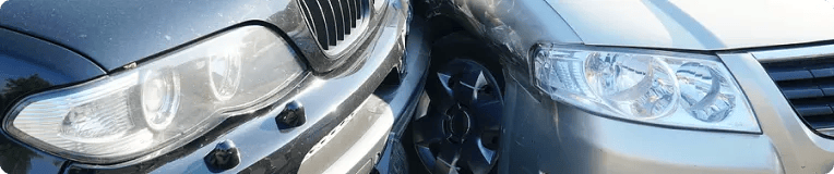 Close-up of the front ends of two cars after a collision, with the bumpers and headlights of both vehicles making contact—a common scene in car accidents that may require guidance from a personal injury attorney.