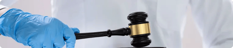 A person wearing a blue medical glove holds a judge’s gavel, poised above a sound block—symbolizing justice in car accidents or personal injury cases, against a light background.