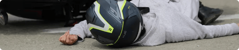 A person wearing a black and yellow motorcycle helmet lies on the ground next to a fallen motorcycle, suggesting an accident on a paved surface—an incident where a personal injury attorney could provide crucial assistance.
