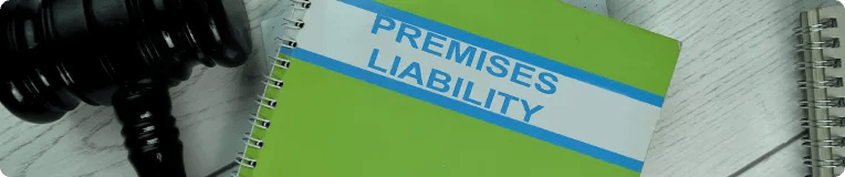 A green spiral-bound notebook labeled "Premises Liability" sits on a light wooden surface next to a judge's gavel and another notebook, hinting at the important work of a personal injury attorney.