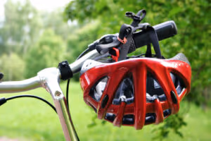 A red bicycle helmet hangs upside down from the handlebars of a silver bike—an important reminder that, like lawyers guide us after car accidents, safety should always come first. Green grass and trees blur softly in the background.