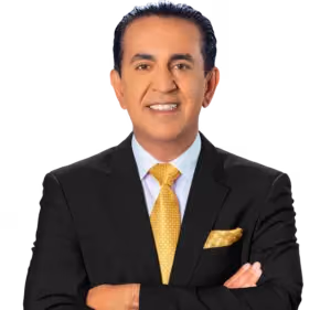 Un hombre en un traje negro con una camisa blanca y una corbata amarilla con patrón sonríe con los brazos cruzados, personificando la confianza de un abogado de lesiones personales de Los Ángeles contra un fondo claro.