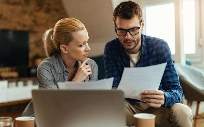 Dos personas revisan documentos financieros frente a una computadora.