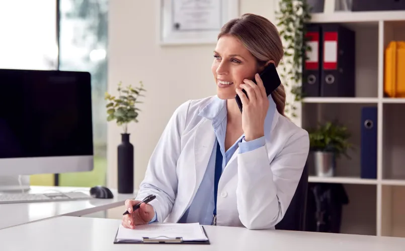Una doctora habla por teléfono mientras toma notas médicas.