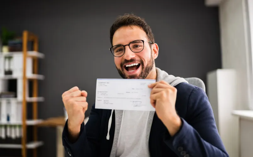 Un hombre sonriente celebra mientras sostiene un cheque.