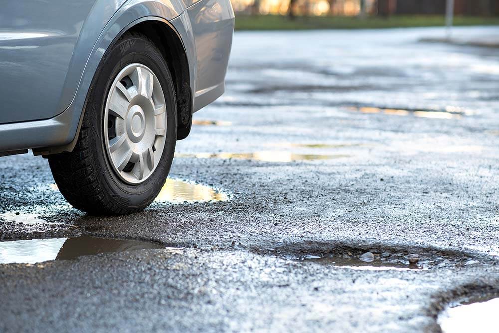 Close-Up-Of-Car-Wheel-On-A-Road-in-Very-Bad-Condition-wth-Large-Potholes-Full-of-Rain-Water