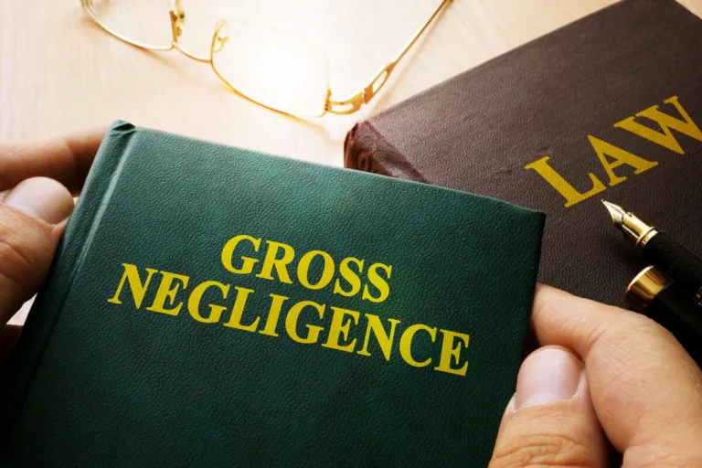 A person holds a green book titled "Gross Negligence" next to a brown book labeled "Law," with glasses and two pens on a wooden table—essential reading for anyone navigating personal injury or seeking a car accident attorney.