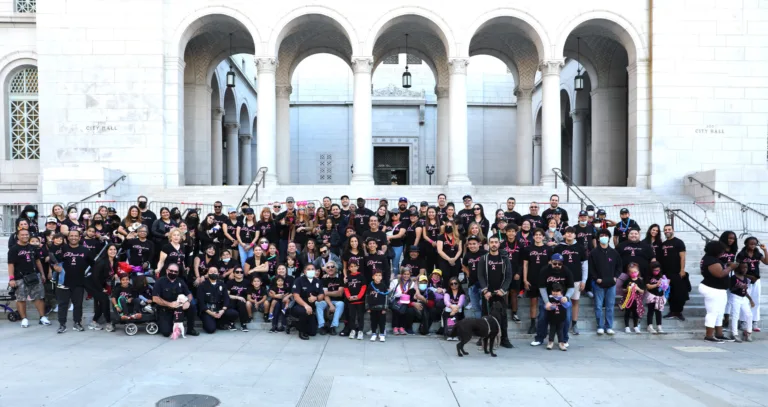 A large group of people, including adults, children, and a dog, pose for a group photo in front of a building with tall arches and steps—many in matching shirts that read "Car Accident Attorneys" to support lawyers who help after car accidents.