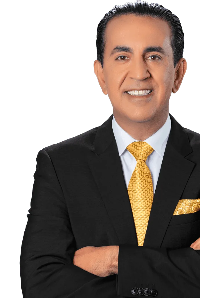 A man in a dark suit with a white shirt, yellow patterned tie, and matching pocket square stands with arms crossed, smiling against a light gray background.