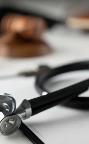 A close-up of a stethoscope lying on a white surface with a blurred judge’s gavel in the background, symbolizing the intersection of healthcare and law, often navigated by personal injury attorneys in car accidents.
