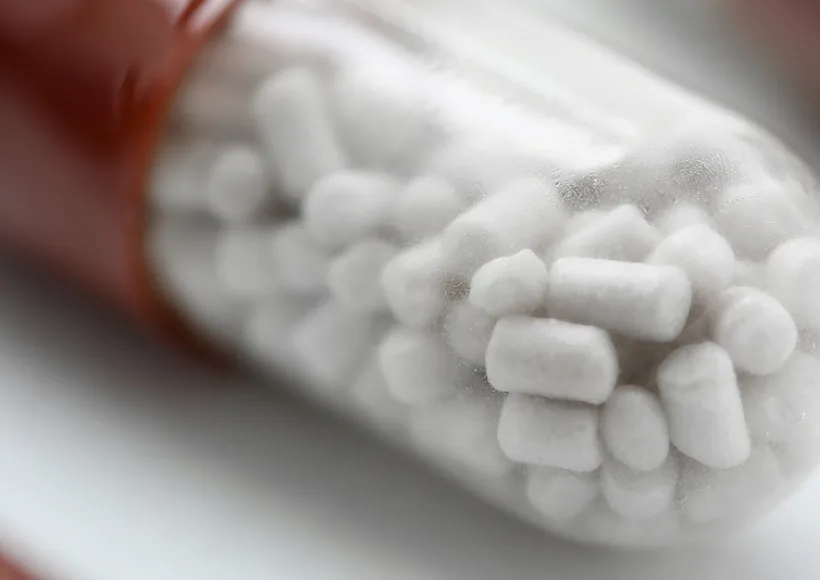 Close-up of a transparent capsule with a red end, filled with small white cylindrical pellets, possibly medication or supplement, often used by lawyers handling personal injury or car accidents cases, against a blurred background.