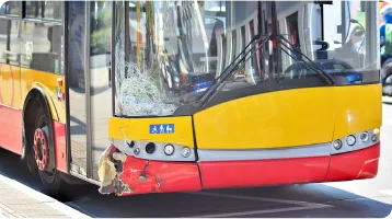 A yellow and red city bus with a damaged front bumper and cracked windshield is parked on a street in daylight, highlighting the aftermath of car accidents that may require the assistance of a personal injury attorney.