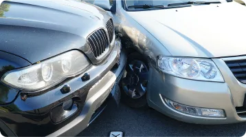 Two cars have collided at the front corners, with the black SUV’s left headlight area pressed against the silver sedan’s right headlight area—an example of car accidents where personal injury lawyers may be needed. Both vehicles are angled on a paved road.