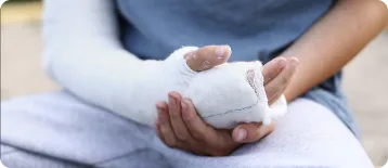 A person wearing a blue shirt and gray pants holds their arm, which is wrapped in a white plaster cast, resting in their lap—perhaps reflecting on whether to consult a personal injury attorney.
