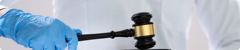 A person wearing a blue medical glove holds a judge’s gavel, poised above a sound block—symbolizing justice in car accidents or personal injury cases, against a light background.