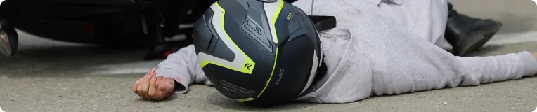 A person wearing a black and yellow motorcycle helmet lies on the ground next to a fallen motorcycle, suggesting an accident on a paved surface—an incident where a personal injury attorney could provide crucial assistance.