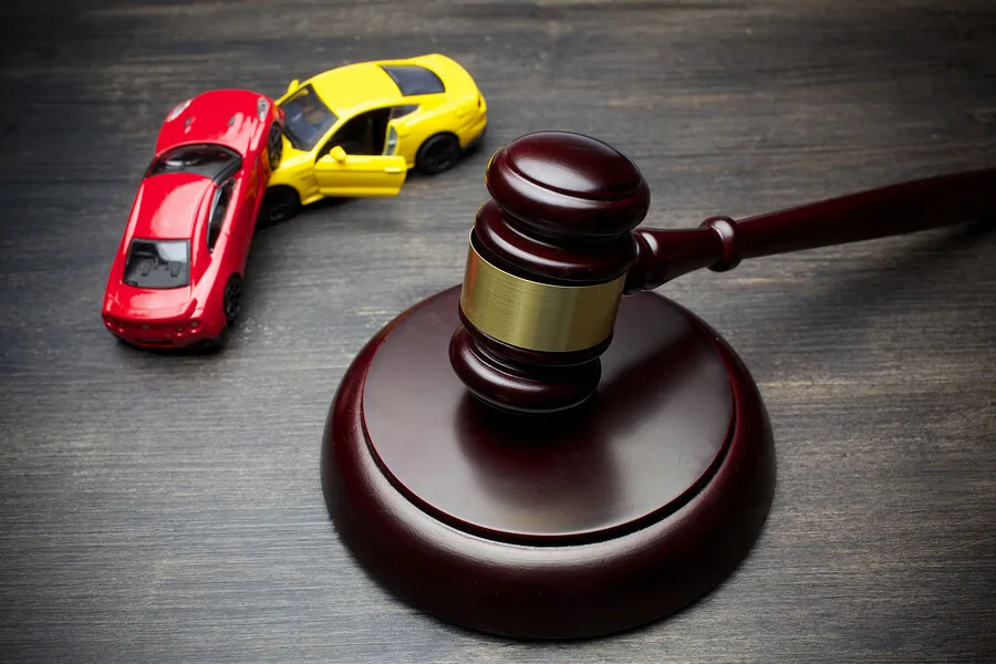 A judge’s gavel rests on a wooden surface next to two toy cars, one red and one yellow, positioned as if they have collided, symbolizing a legal case where personal injury attorneys and lawyers may be involved.