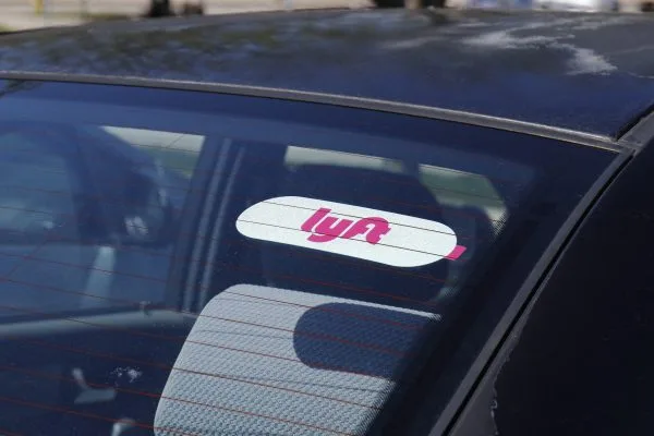 A pink and white Lyft sticker is displayed on the rear window of a car, viewed from outside—reminding passengers that if car accidents occur, consulting personal injury attorneys or lawyers can help protect your rights.