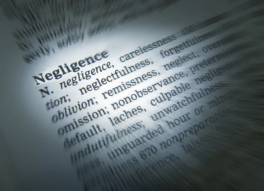 Close-up of a dictionary page focused on the word "Negligence," with its definition and related terms—carelessness, neglectfulness, omission, and culpable indifference—highlighted in the center, often referenced by personal injury attorneys and lawyers.