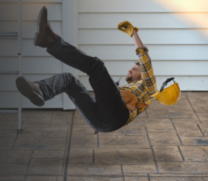 A construction worker in a yellow plaid shirt and gloves falls backward from a ladder, his hard hat flying off onto the tiled floor outside a building with white siding—an incident where a personal injury attorney could help protect your rights.