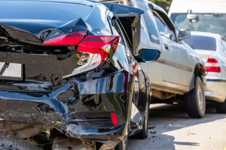 A close-up view of a black car with significant rear-end damage from a multi-car accident, with other vehicles visible in the background on a sunny day—a scene where car accident attorneys often help navigate legal claims.