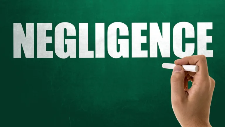 A hand holding a piece of chalk writes the word "NEGLIGENCE" in large, bold white letters on a green chalkboard background, highlighting an important concept for lawyers handling personal injury and car accidents cases.