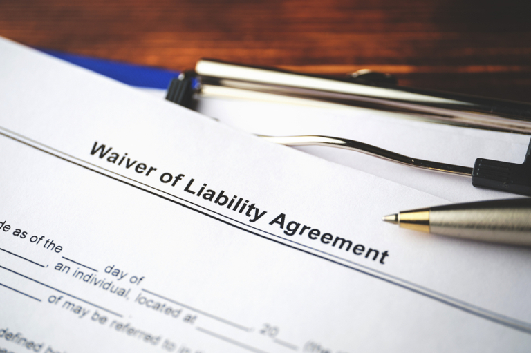 A close-up of a "Waiver of Liability Agreement" document on a desk, partially filled out, with a silver pen and a pair of black-framed eyeglasses—often used in cases involving car accidents or personal injury—placed on top.