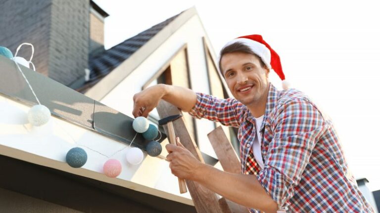 Man-In-Santa-Hat-Decorating-House-with-lights-on-ladder