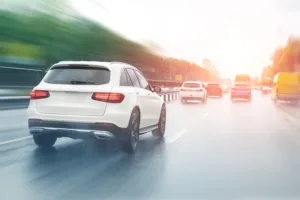 A white SUV drives on a wet, multi-lane road with blurred cars and trees, suggesting motion—an important scene for lawyers specializing in car accidents, as busy roads like this often lead to legal cases.