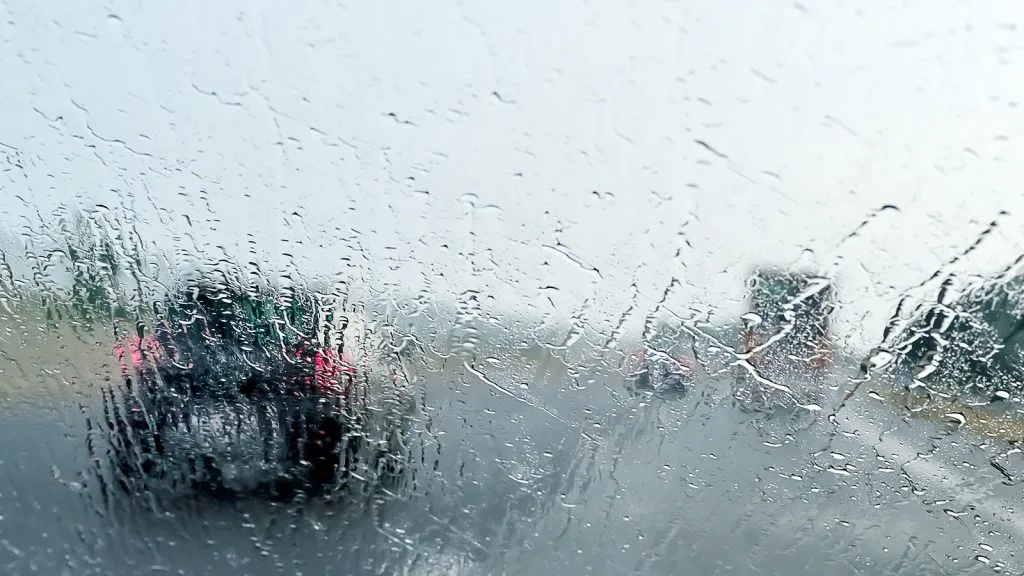 A view through a car windshield covered in rain, with blurred vehicles visible ahead on a wet road, creating a hazy effect—an all-too-common scene that personal injury lawyers or a car accident attorney may often encounter.