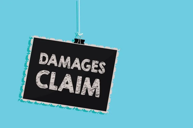 A black sign with the words "DAMAGES CLAIM" in bold white letters hangs against a light blue background, highlighting the importance of personal injury cases.