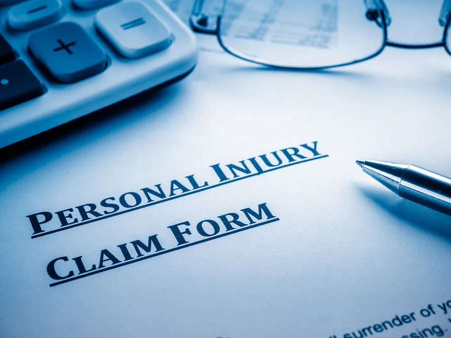 A close-up of a personal injury claim form on a desk, with a pen resting on it, partial view of a calculator, and eyeglasses nearby—perfect for illustrating the work of a personal injury attorney.