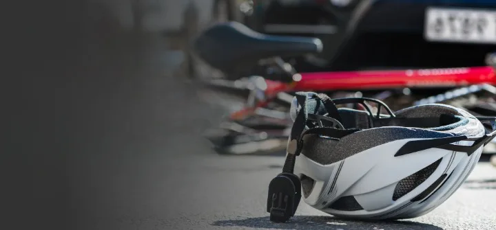 A white bicycle helmet lies on the ground in front of a fallen red bike, with a blurred car and license plate in the background, evoking the aftermath of car accidents and highlighting the potential for personal injury.