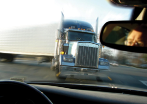 View from inside a car as a large semi-truck approaches head-on at high speed, evoking the danger of car accidents. A person’s reflection is visible in the rearview mirror, highlighting moments that may require a personal injury attorney.