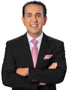 A car accident attorney in a black suit, white shirt, and pink patterned tie stands with his arms crossed, smiling at the camera. He has short dark hair and a matching pink pocket square against a plain white background.
