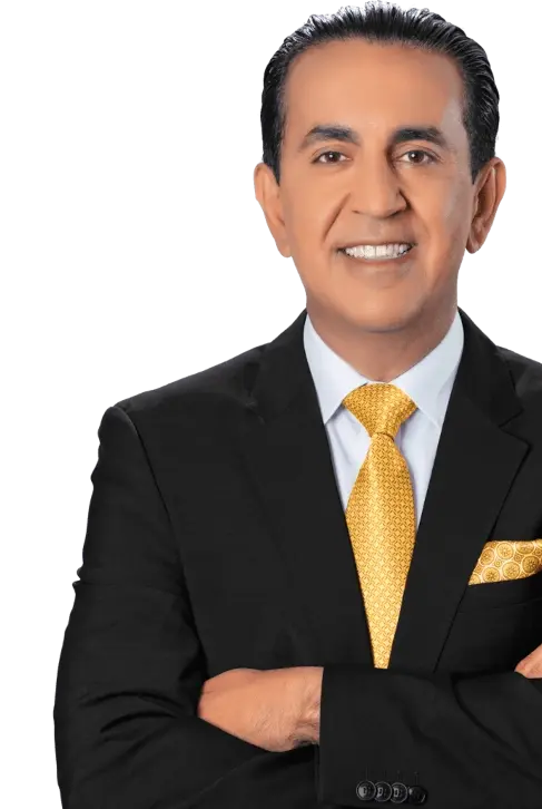 A man in a black suit with a white shirt, yellow patterned tie, and matching yellow pocket square stands with arms crossed, smiling at the camera against a plain background.