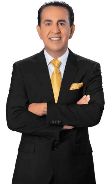 A man in a black suit with a yellow tie and matching pocket square stands with arms crossed, smiling at the camera.