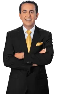 Man in a black suit with a yellow tie and matching pocket square, smiling with arms crossed, standing against a transparent background.