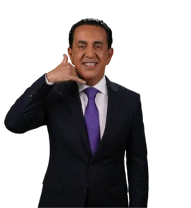 A man in a dark suit and purple tie smiles while making a "call me" gesture with his hand, holding his thumb and pinky finger to his face. The background is plain white.