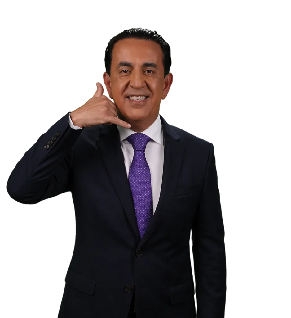 A man in a dark suit and purple tie smiles while making a "call me" gesture with his right hand against a plain white background.